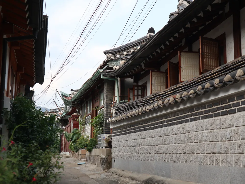 A quiet Bukchon side lane with the curved tiled eaves of a hanok, latticed windows and a stone-and-brick wall
