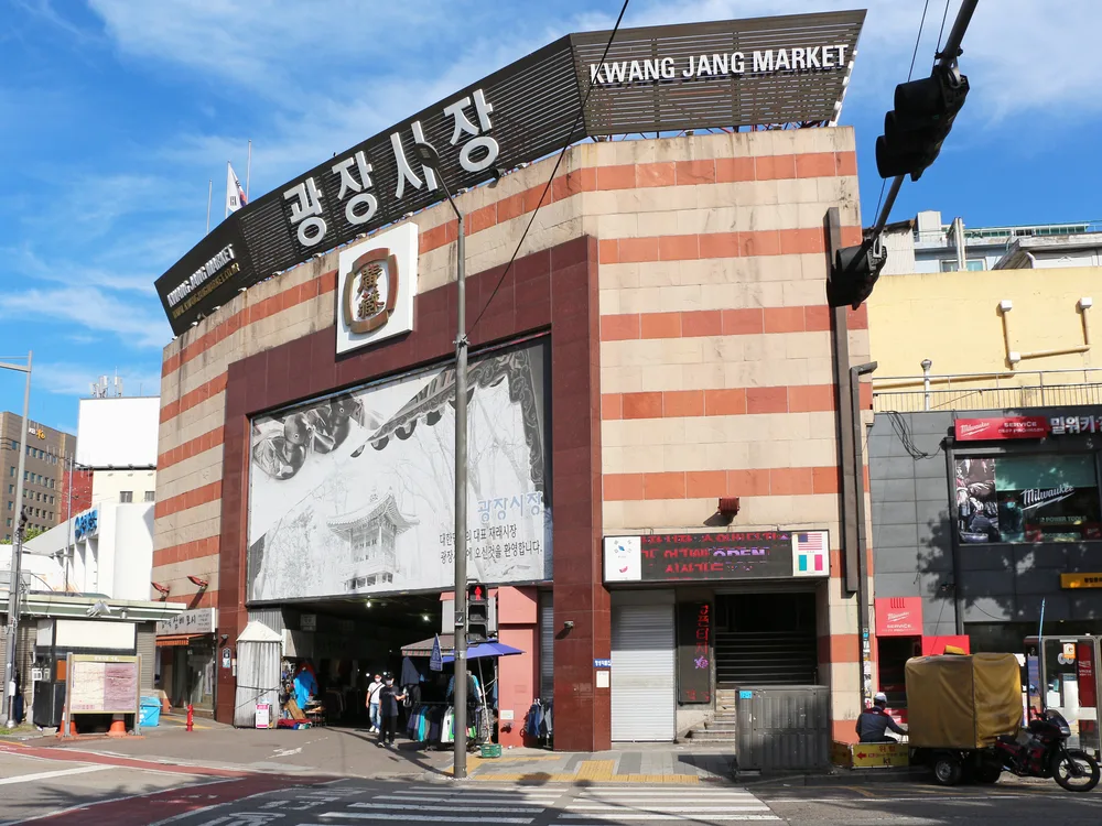 The street-corner entrance of Gwangjang Market under a large sign reading Kwang Jang Market in Korean and English
