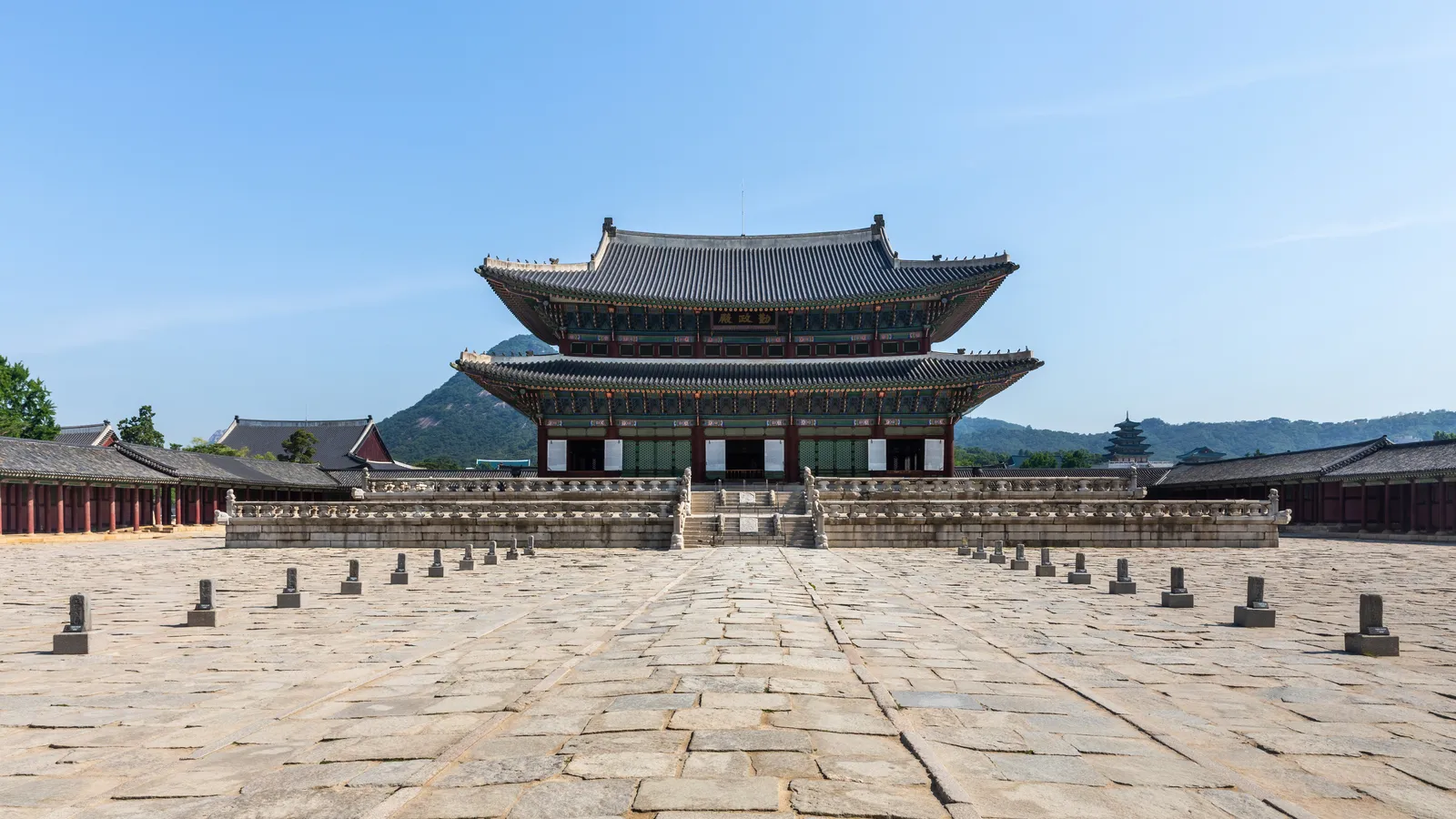 The Geunjeongjeon throne hall at Gyeongbokgung Palace on its stone terrace, with Bugaksan mountain behind under a clear sky
