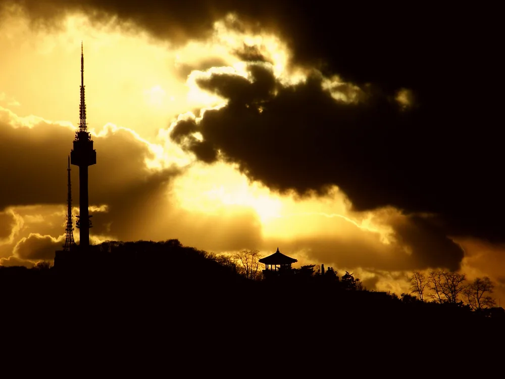 N Seoul Tower and a small pavilion silhouetted on the Namsan ridge against a dramatic golden sunset sky