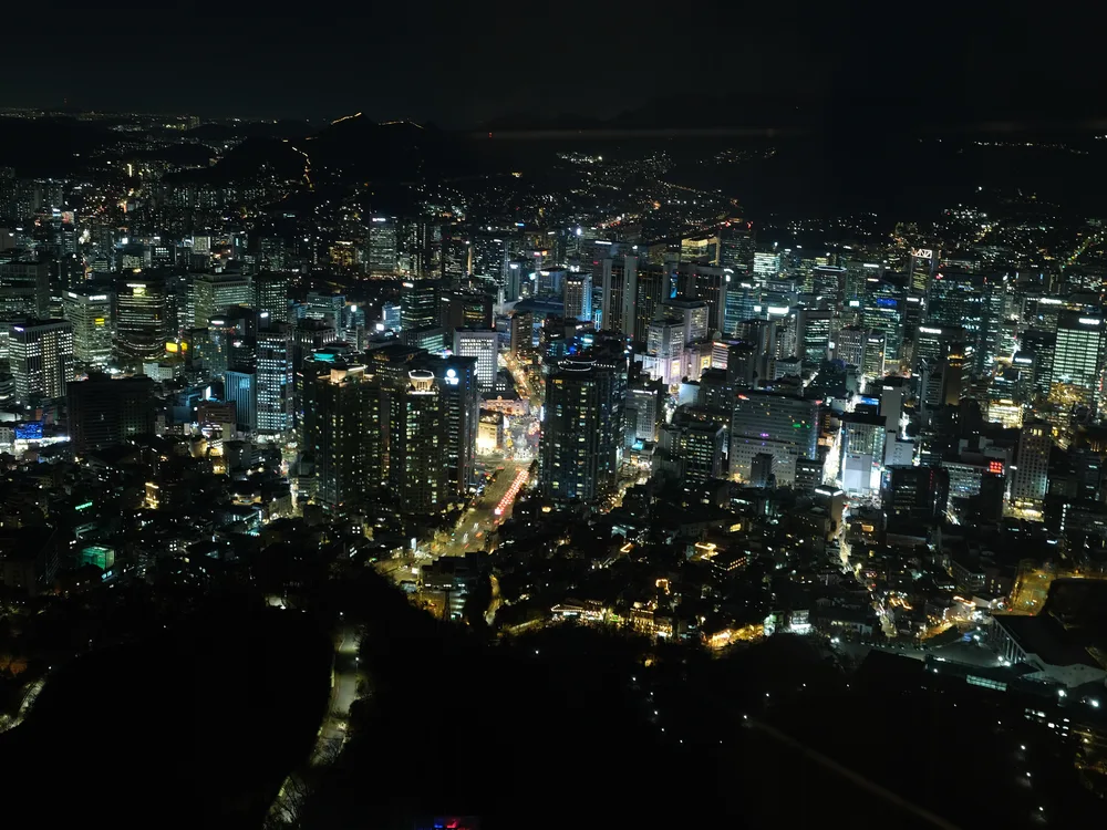 The night view over central Seoul from the N Seoul Tower observation deck, a dense field of city lights with dark hills beyond