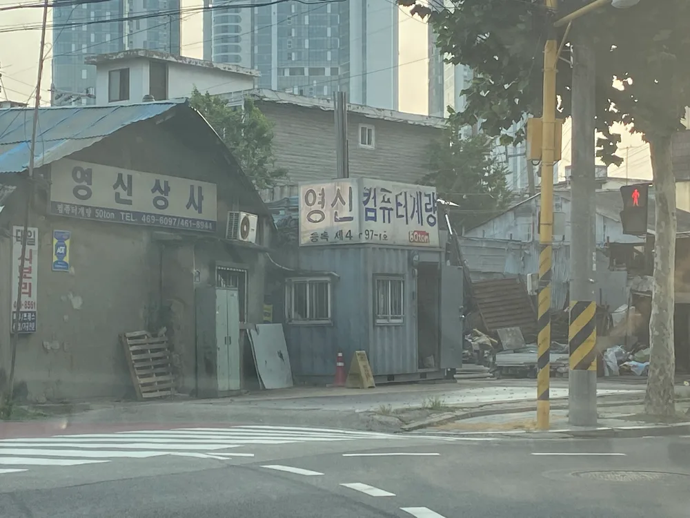 Low old workshops with hand-painted signs in Seongsu-dong, high-rise apartment towers rising directly behind them