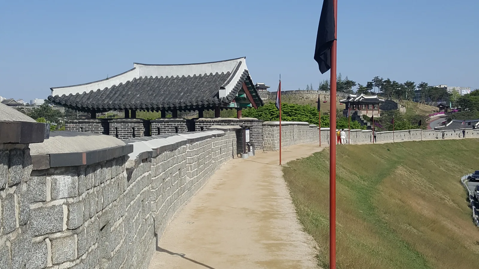 A stone rampart and tiled guard pavilion along the walls of Hwaseong Fortress in Suwon under a clear sky