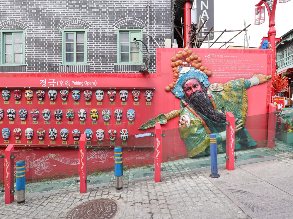 A red wall on the Samgukji street with Peking Opera masks and a large relief of a Three Kingdoms warrior