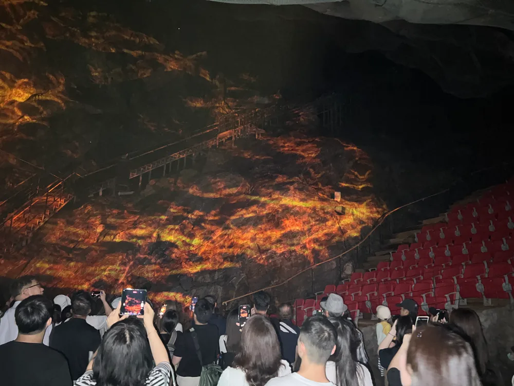A projection-mapping light show on the cave rock face above rows of red seats