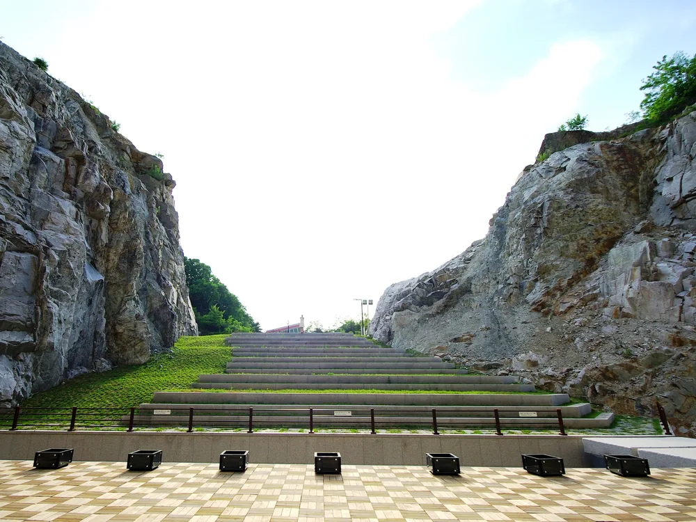Grassed amphitheatre steps rising between the cut-granite walls of the old quarry