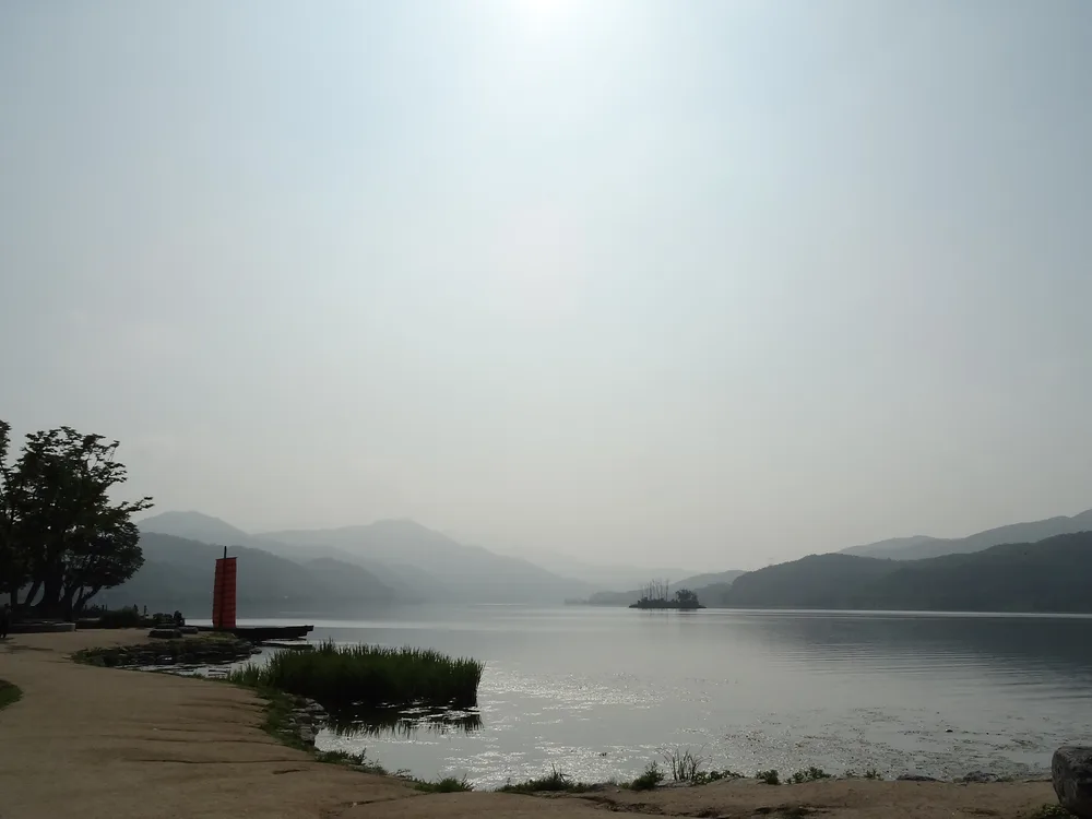 A hazy morning over the river confluence at Dumulmeori, with a red-sailed traditional boat moored by the bank