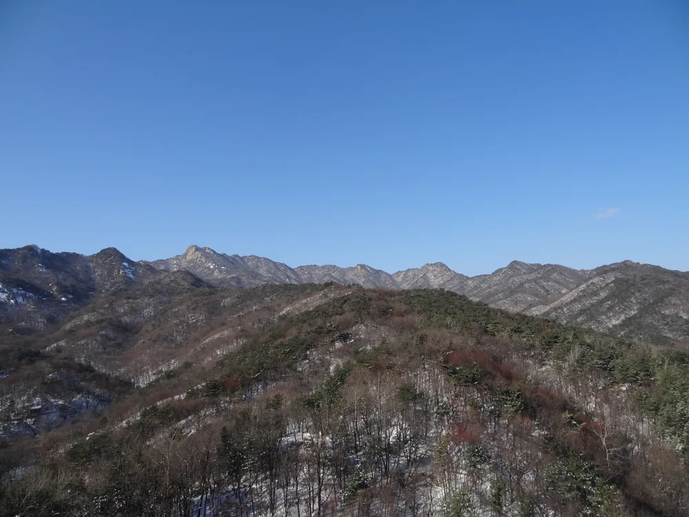 Snow-dusted ridgelines of Bukhansan under a clear blue winter sky, bare forest below
