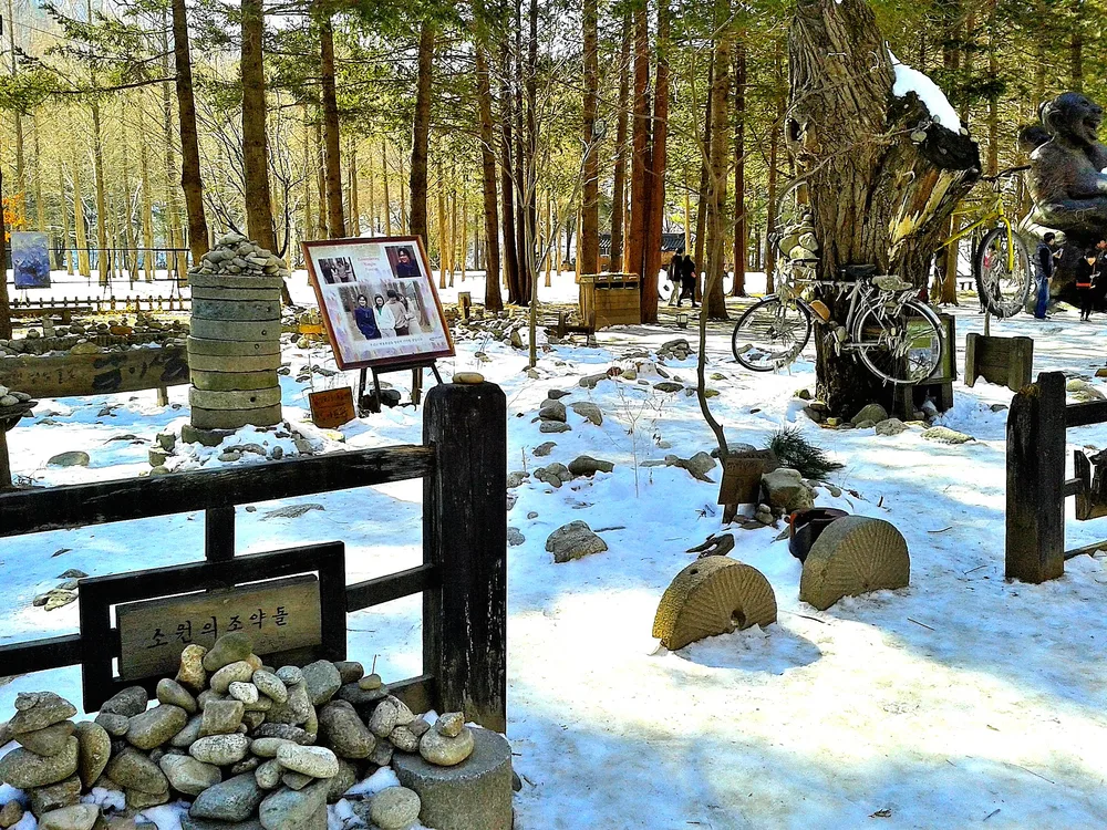 A snowy corner of Nami Island with a Winter Sonata display, a white-painted bicycle and wish-stone cairns