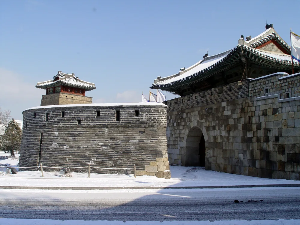 Hwaseomun gate and the round Seobuk Gongsimdon bastion at Hwaseong Fortress, snow on the tiled roofs and the ground