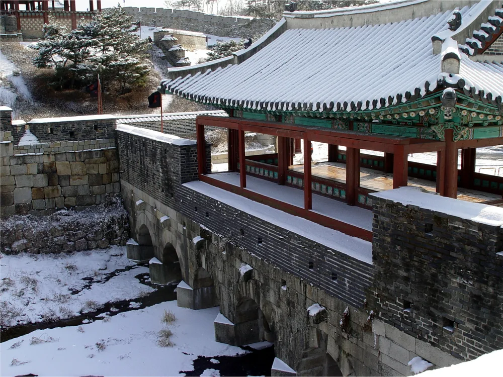 The Hwahongmun water gate and its pavilion at Hwaseong, snow on the roof and the frozen stream running under the arches