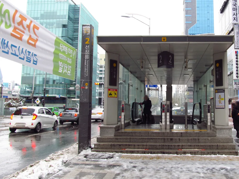 A street-level Seoul subway entrance with a large cube sign reading 2 EXIT above the escalator down