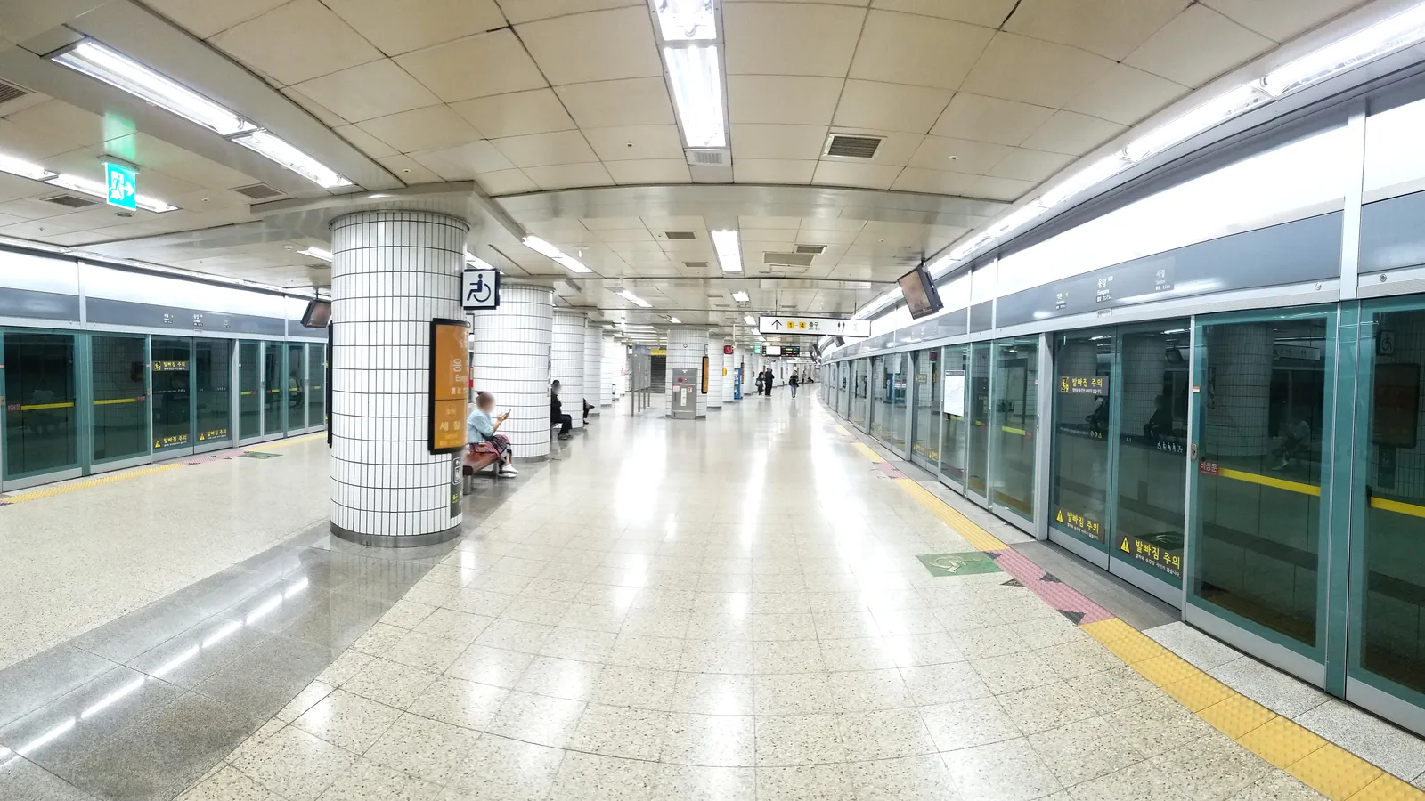 A clean, near-empty Seoul metro platform with full-height platform screen doors and overhead direction signs