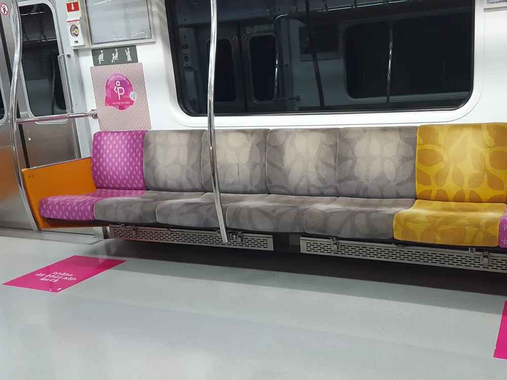 The end of a Seoul metro bench with bright pink priority seats for pregnant passengers, marked with pink signs and floor decals
