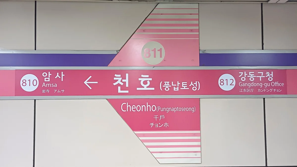 A pink Seoul Metro platform sign for Cheonho station, marked 811, with Amsa (810) to the left and Gangdong-gu Office (812) to the right