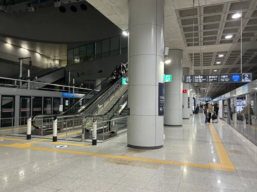 An AREX all-stop train platform at Incheon Airport, with a blue overhead sign listing the stops Geomam, Gimpo Airport, Hongik Univ and Seoul Station