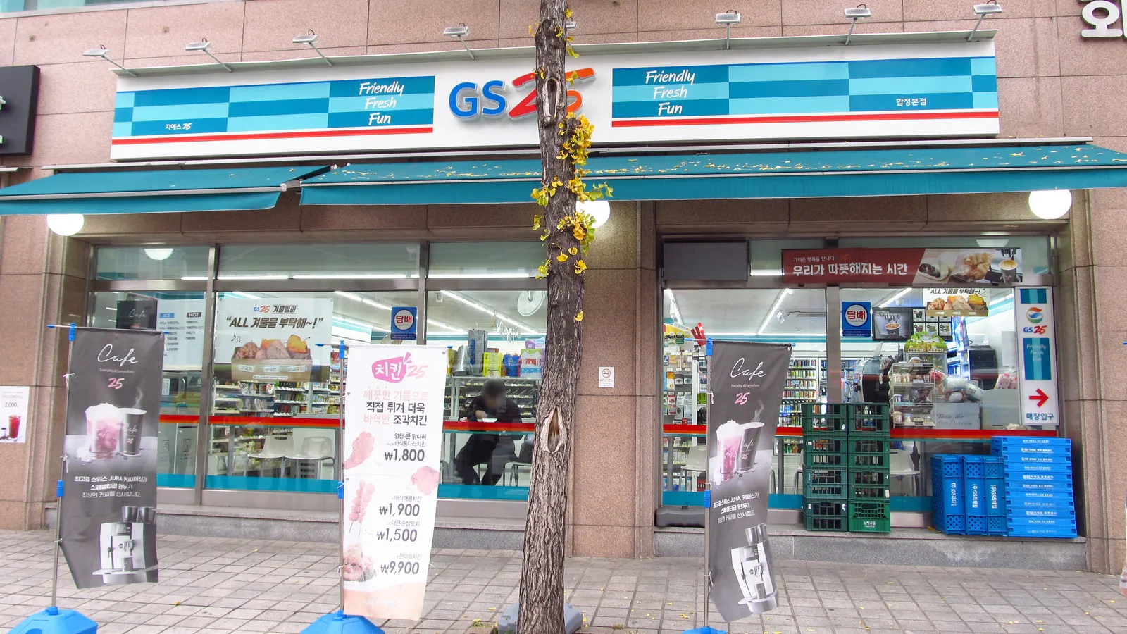 The blue-and-white storefront of a GS25 convenience store in Seoul, with promo banners and a window counter for eating in