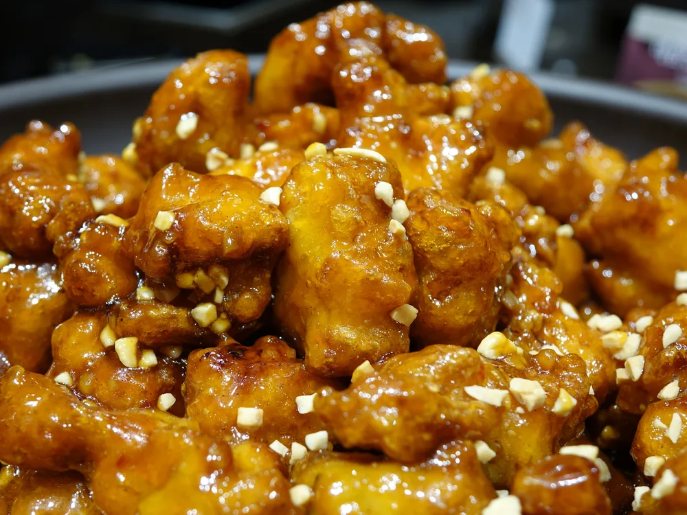 A mound of bite-sized dakgangjeong chicken in a glossy amber glaze, topped with chopped peanuts