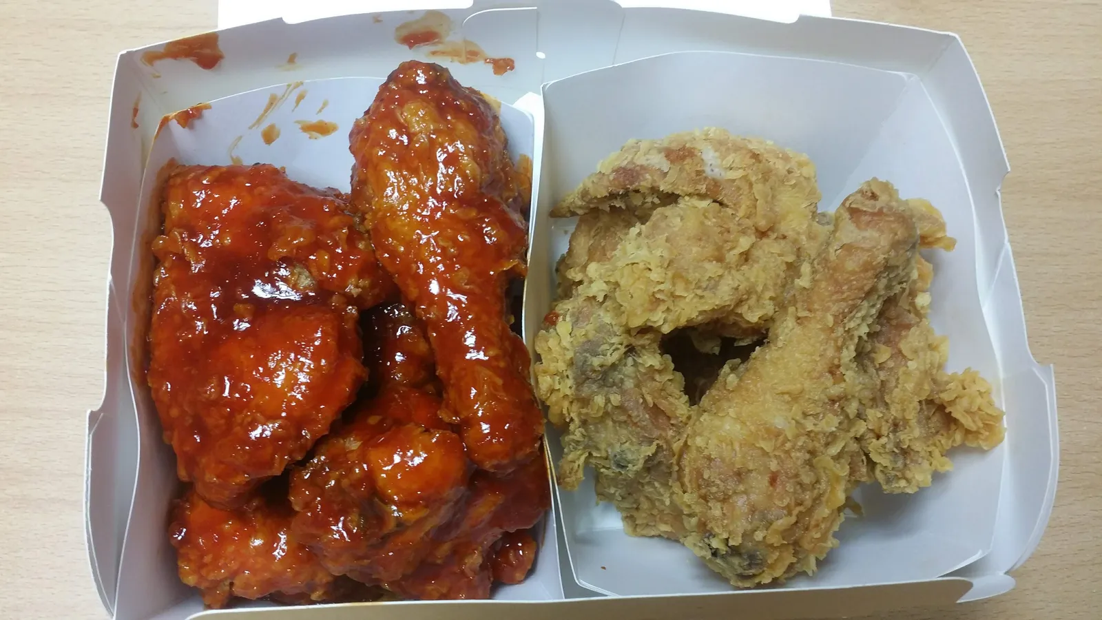 A takeout box split in two — glossy red yangnyeom chicken on one side, plain golden fried chicken on the other