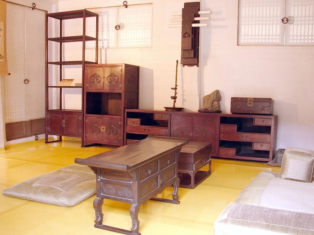 A restored hanok room with a glossy oiled-paper floor, a low writing desk, floor cushions and a rolled sleeping mattress against the wall